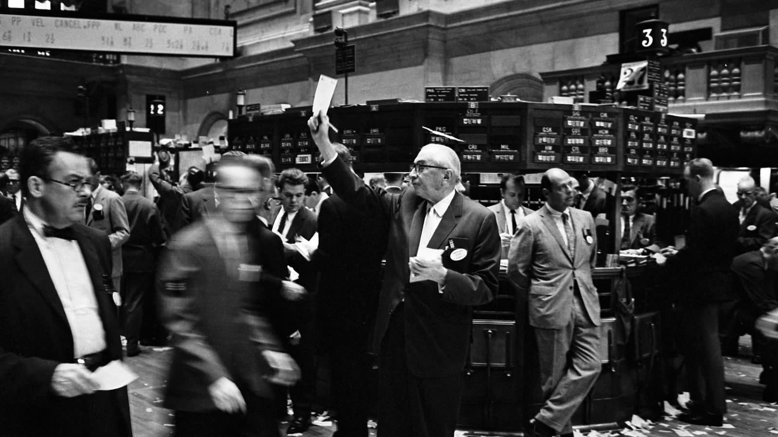 Stock brokers working on the New York Stock Exchange trading floor in a documentary black-and-white photograph.
