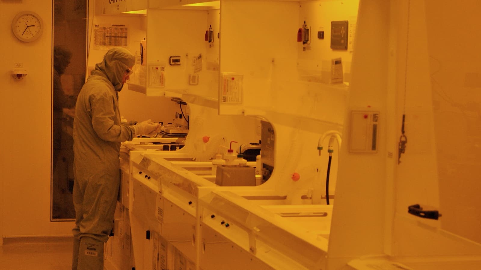 Scientists work under orange safety lighting in a semiconductor photolithography cleanroom