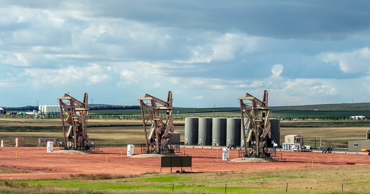 Three oil pumpjacks operating in a North Dakota field under a cloudy sky.