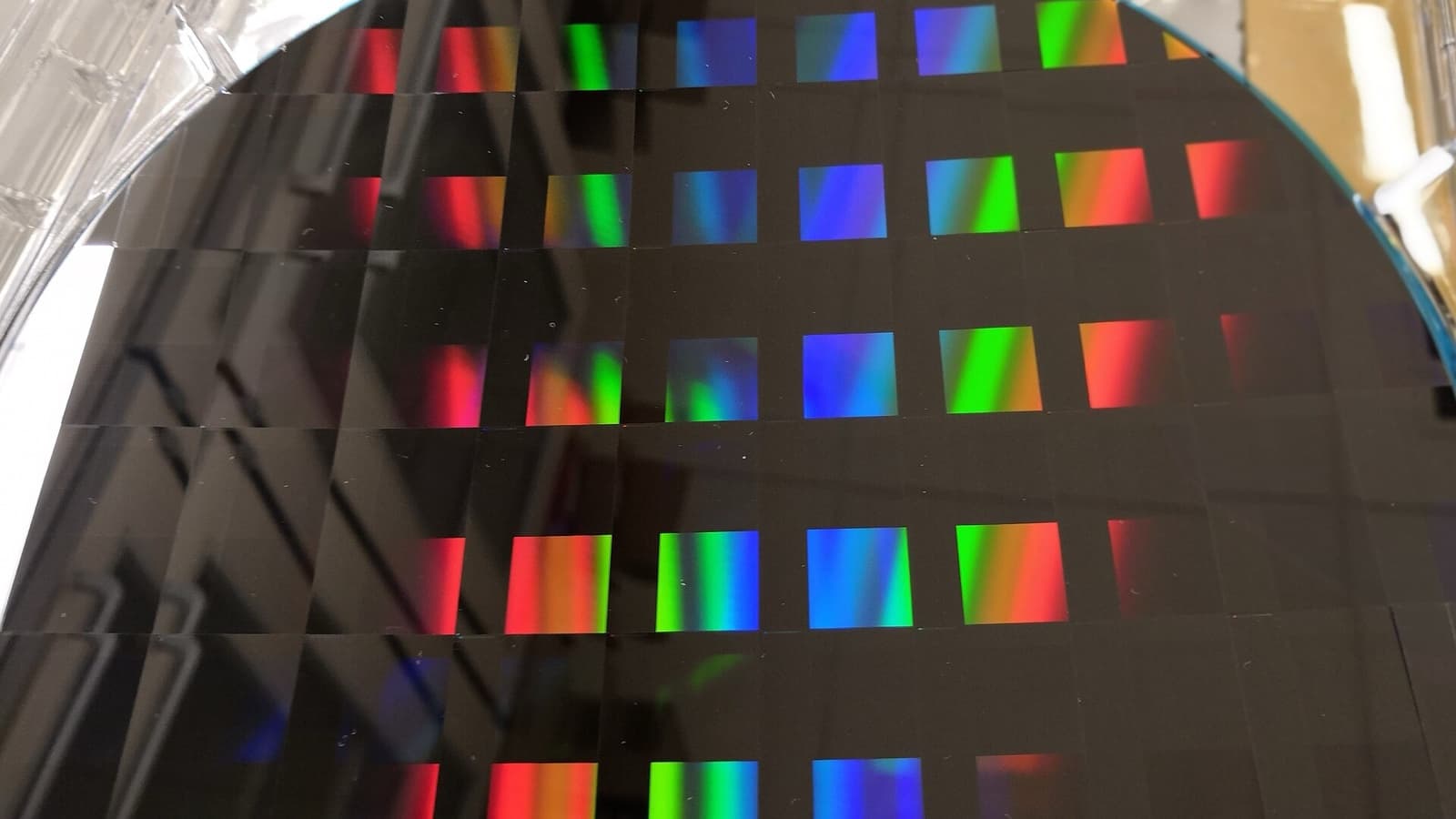 Close-up photograph of a patterned silicon wafer splitting light into coloured reflections.