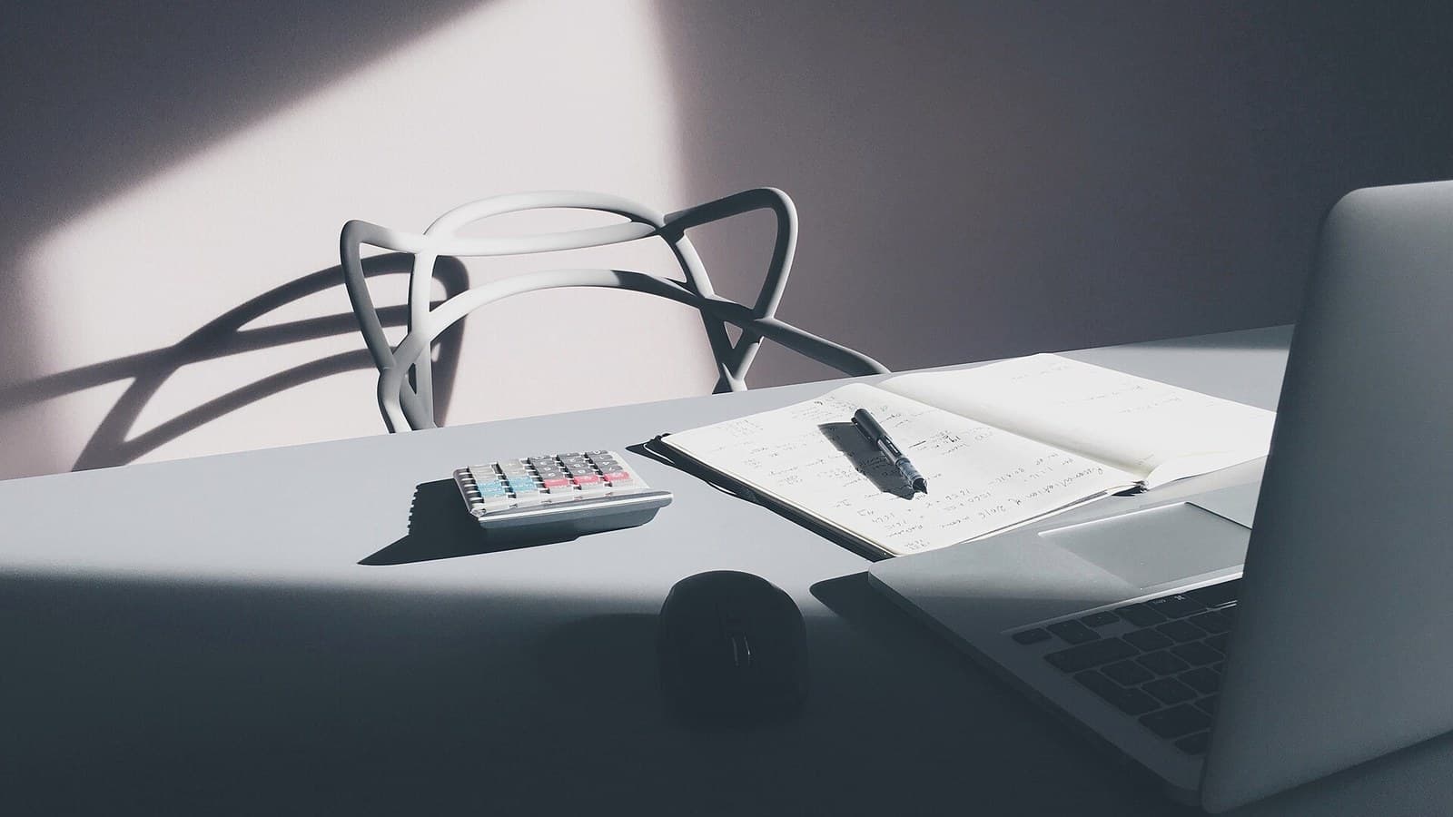 Laptop, notebook and calculator on a wooden desk used for working through numbers