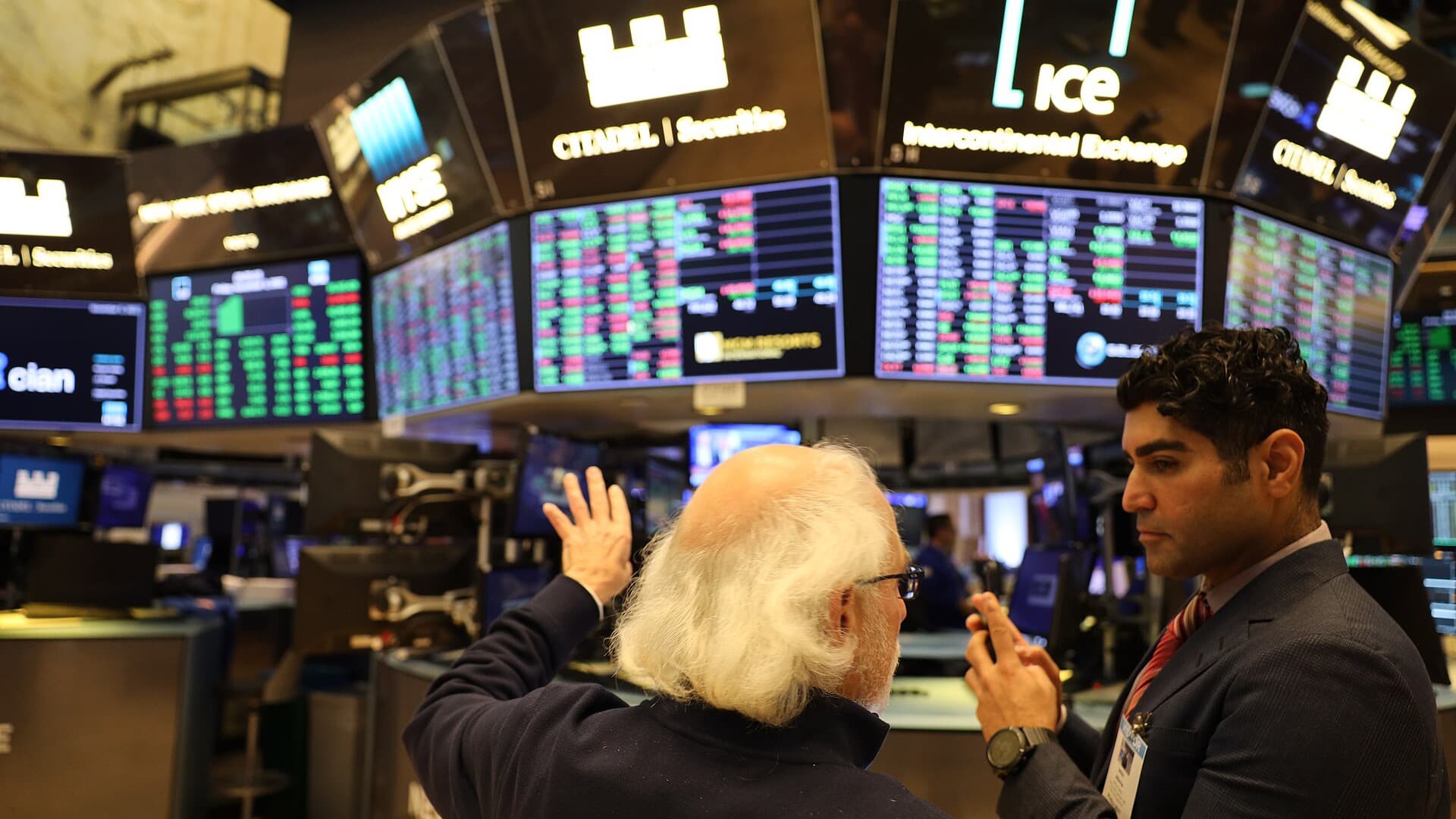 Two people discuss market data on the New York Stock Exchange trading floor