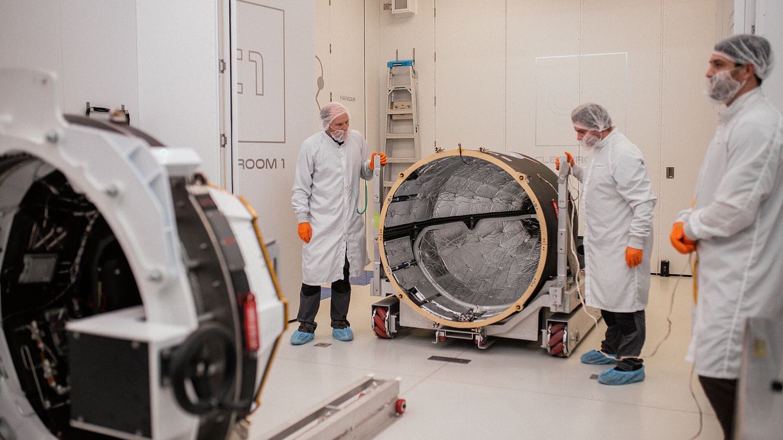 Cleanroom technicians stand around cylindrical spacecraft hardware at a Rocket Lab facility