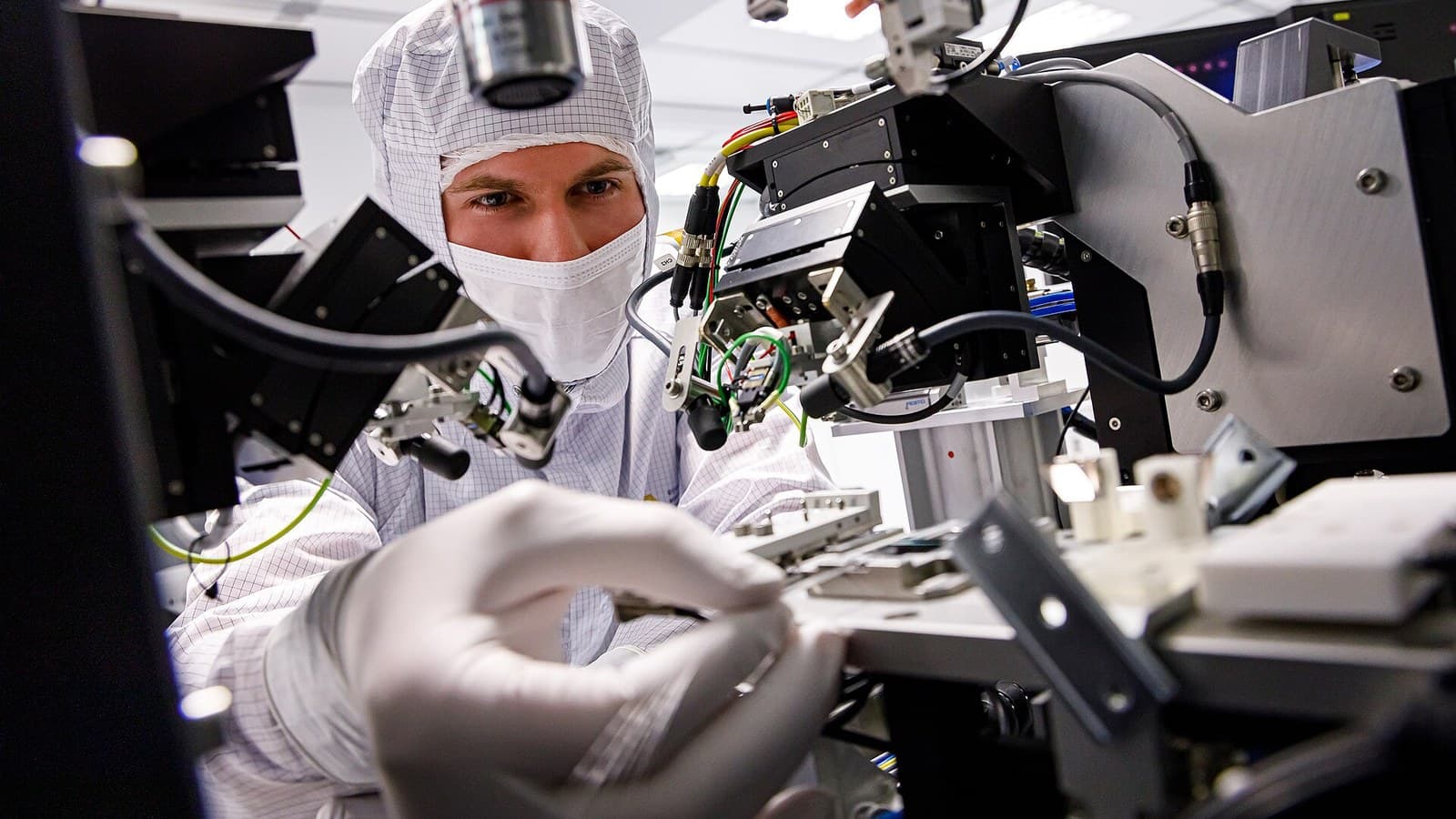 A cleanroom researcher adjusts precision photonics equipment and cabling