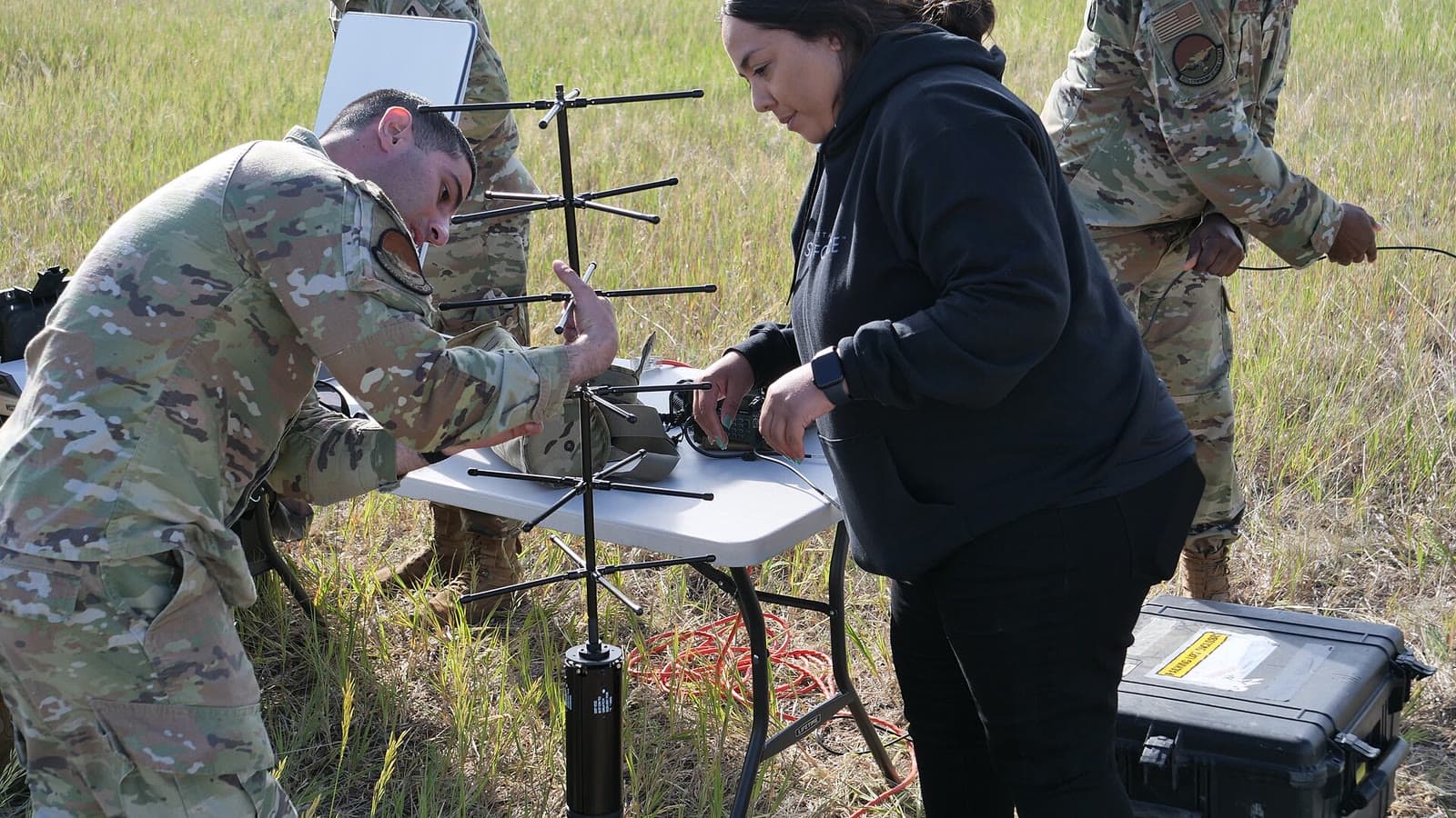 Space Force personnel and a civilian specialist assemble a portable satellite ground-station antenna in a field