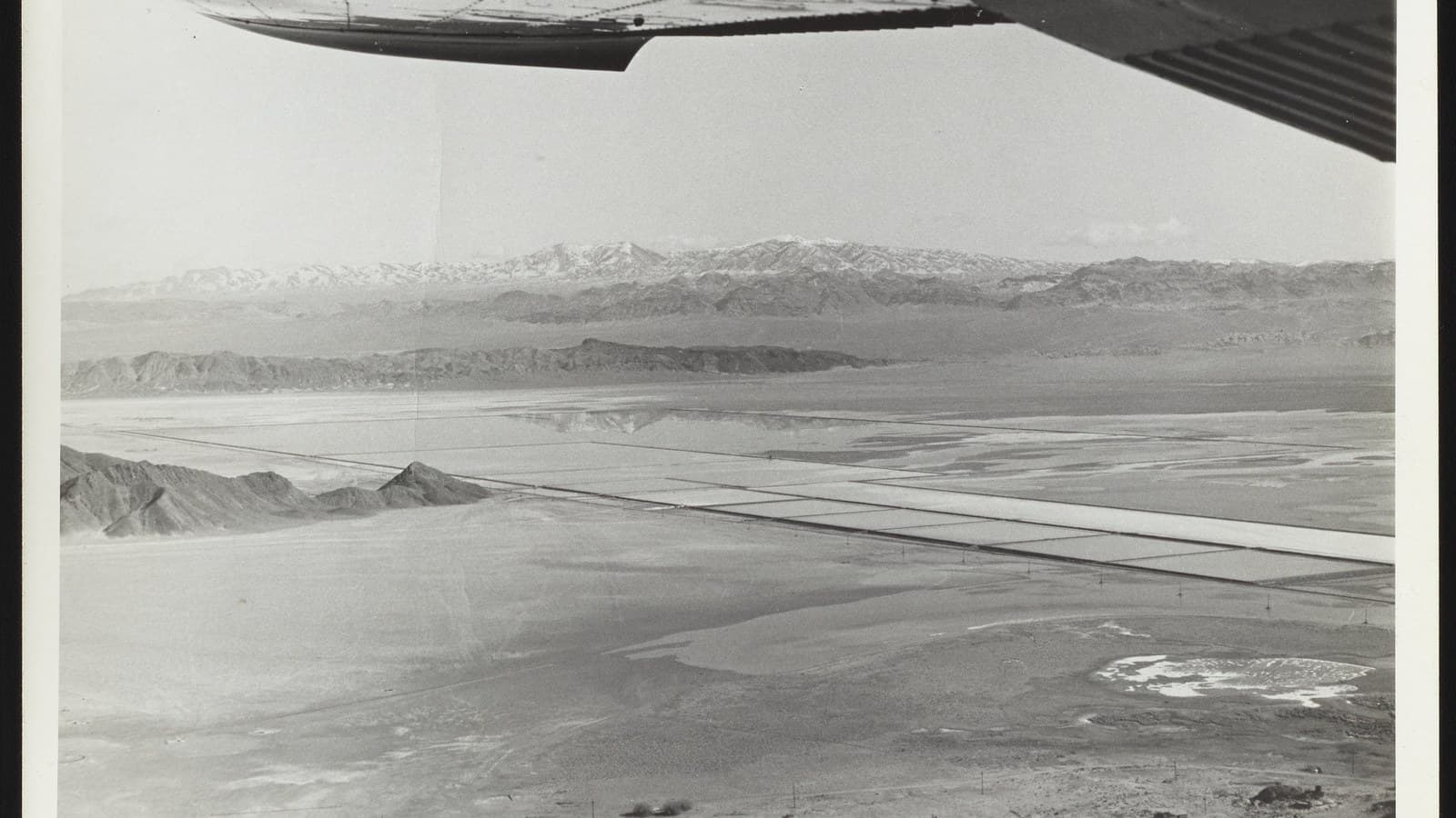 Black-and-white aerial photograph from an aircraft showing lithium brine evaporation panels and mountains at Silver Peak, Nevada