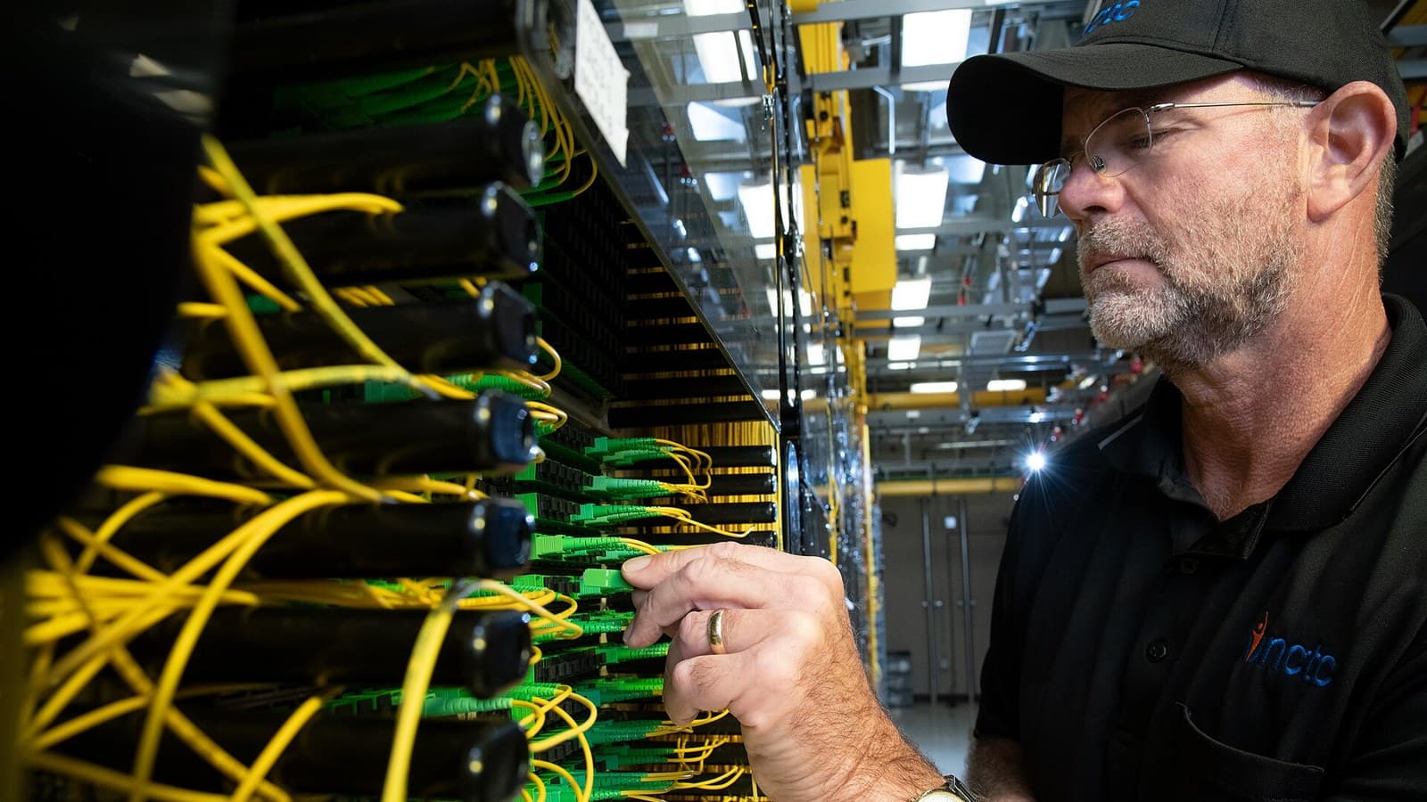 A technician connects yellow fiber-optic jumper cables in a data-centre network rack