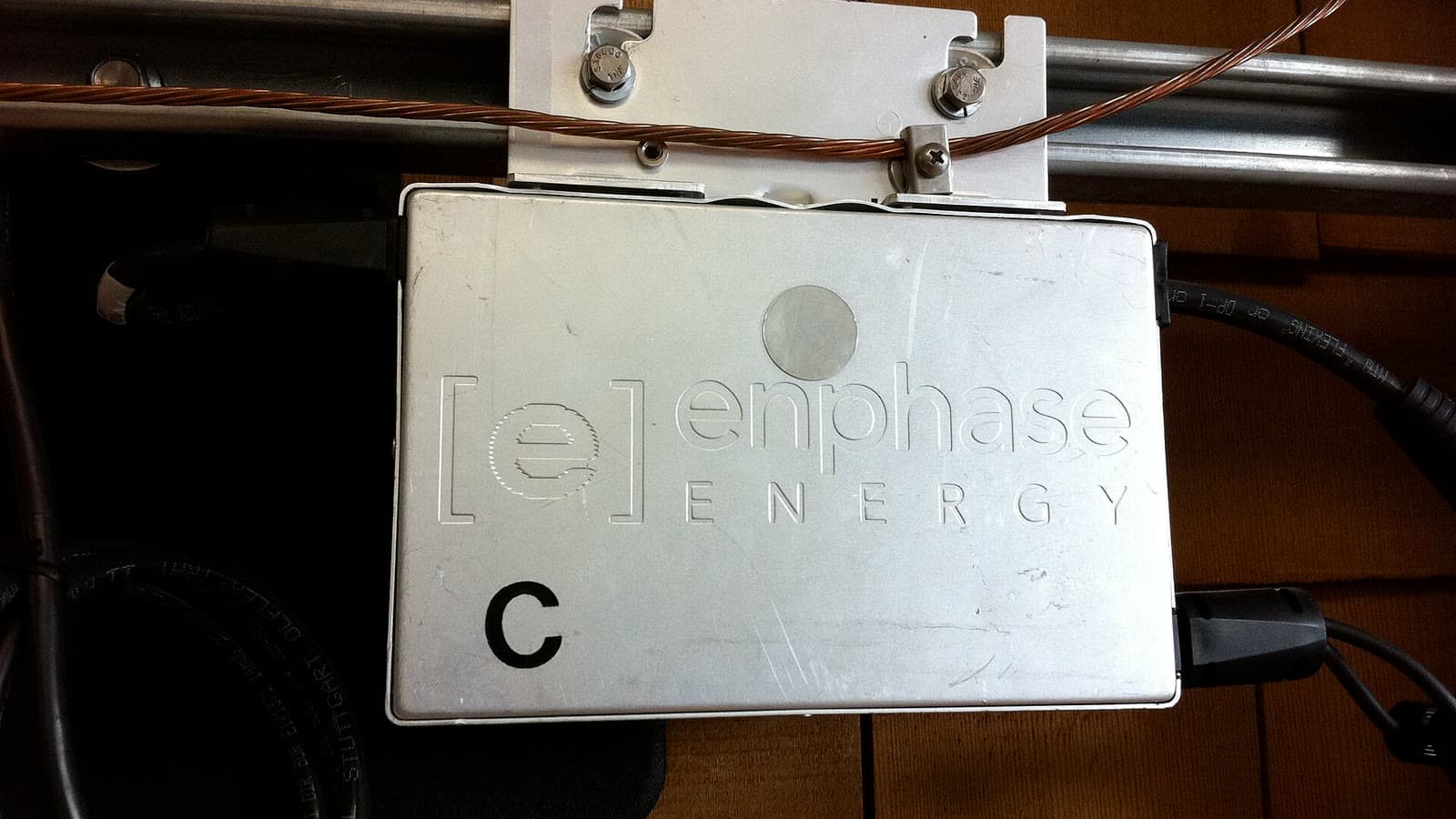 An Enphase M190 solar microinverter mounted beneath a panel rail during installation