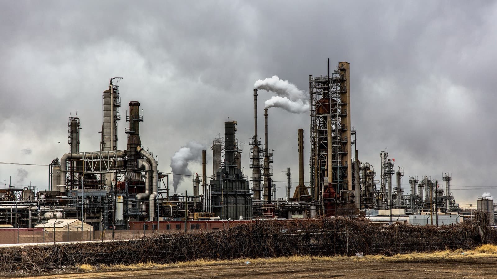 A sprawling petroleum refinery with process towers and steam under an overcast sky