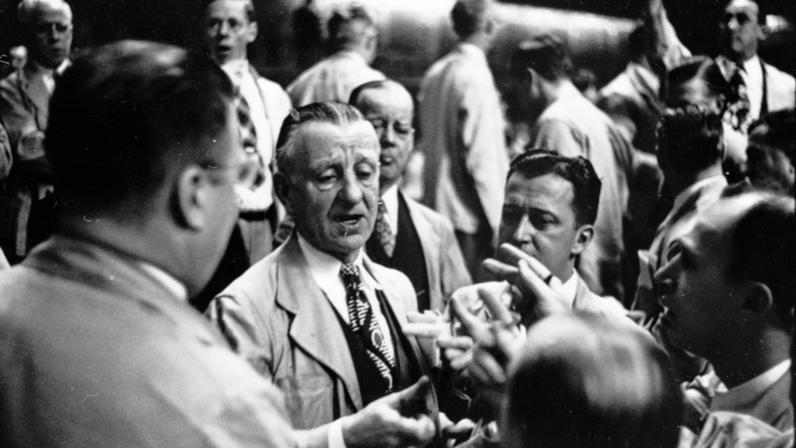 Archival black-and-white photograph of traders in suits gesturing on the Chicago Board of Trade floor.