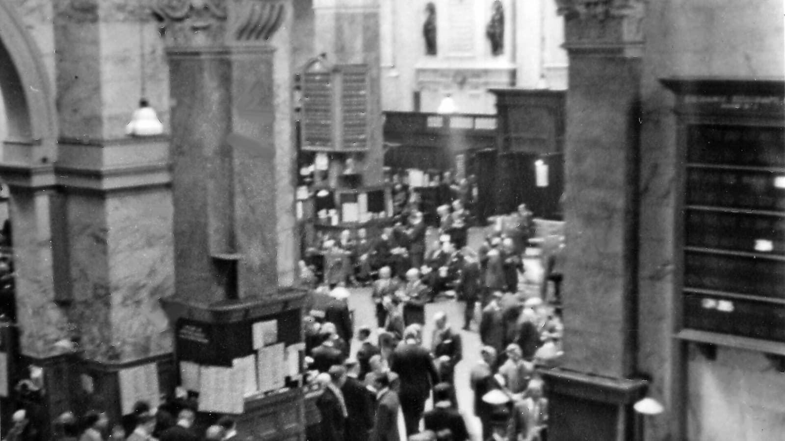 Archival photograph of crowds among large columns on the London Stock Exchange trading floor
