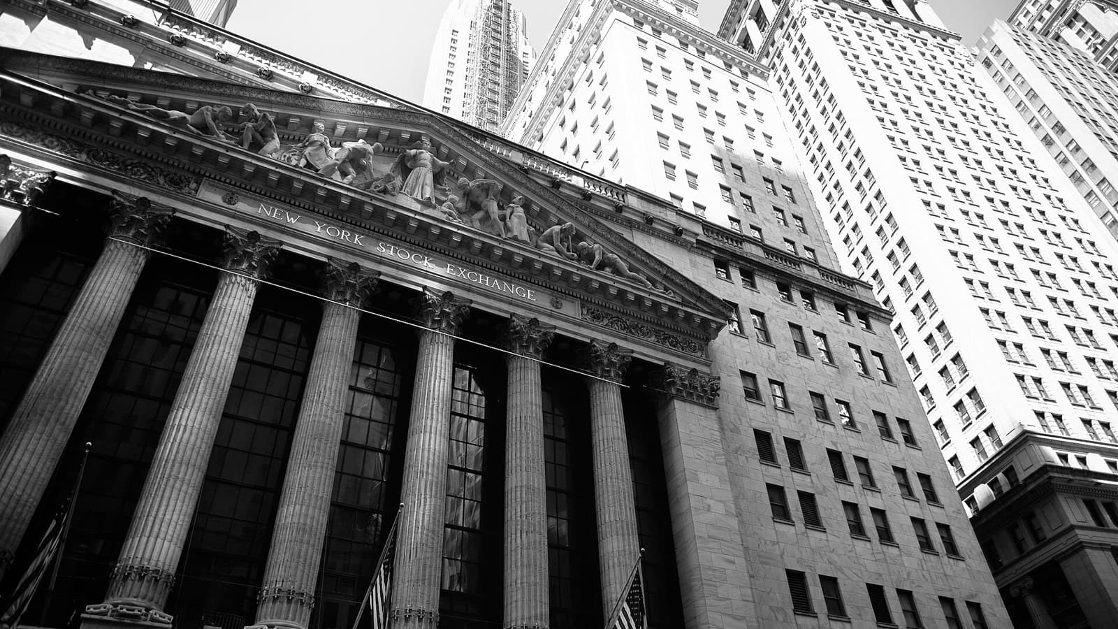 Black-and-white view of the New York Stock Exchange’s columned façade and surrounding skyscrapers